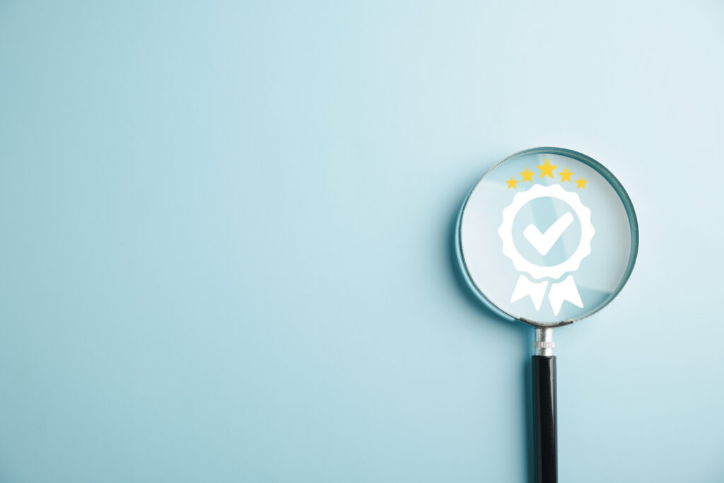 Forstørrelsesglas, der fremhæver et kvalitetsstempel med flueben - symbol på ISO 9001 og kvalitetssikring.